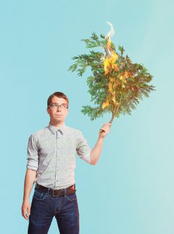 Eric Kennedy looking at a tree branch he is holding that is on fire