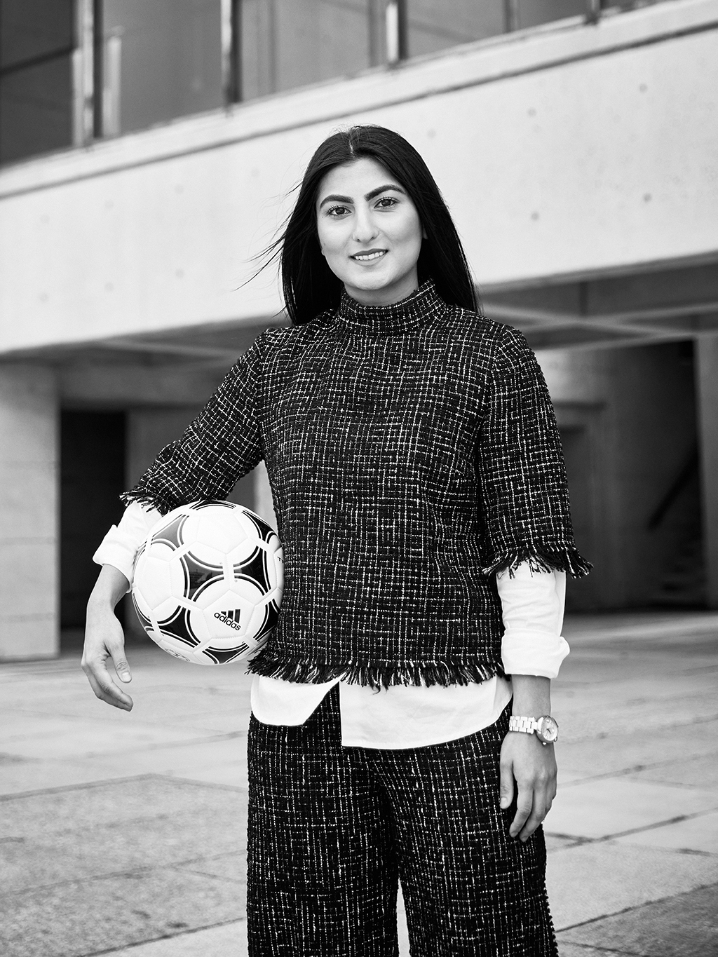 Farkhunda Muhtaj staying outside on York University podium, smiling, soccer ball under her arm
