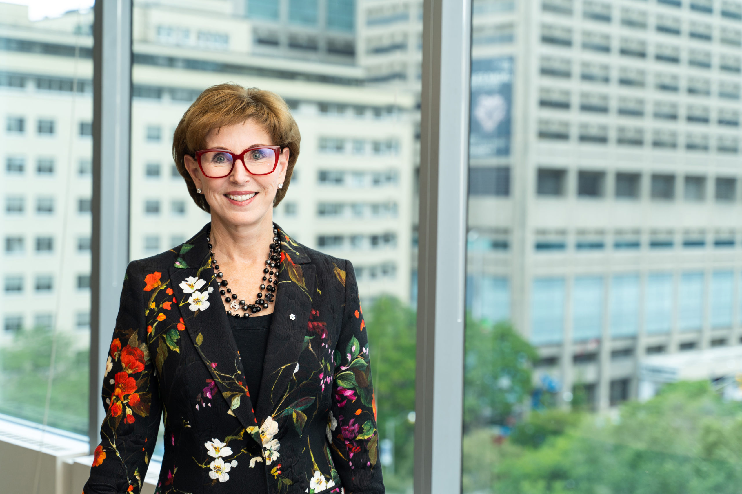 Kathleen (Katie) Taylor smiling, in front of a window overlooking office buildings