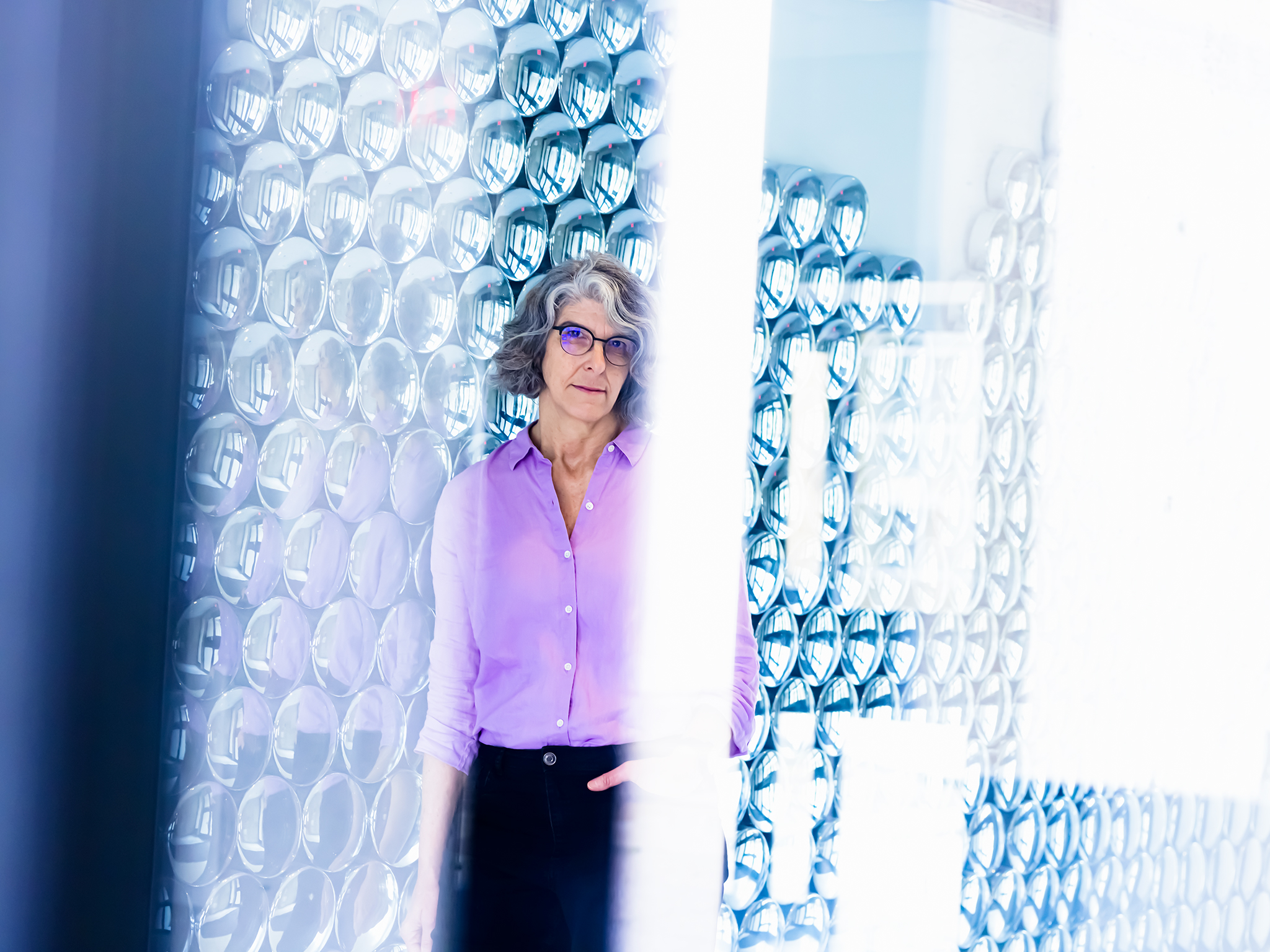 Deborah Harris standing in front of wall of small circular mirrors