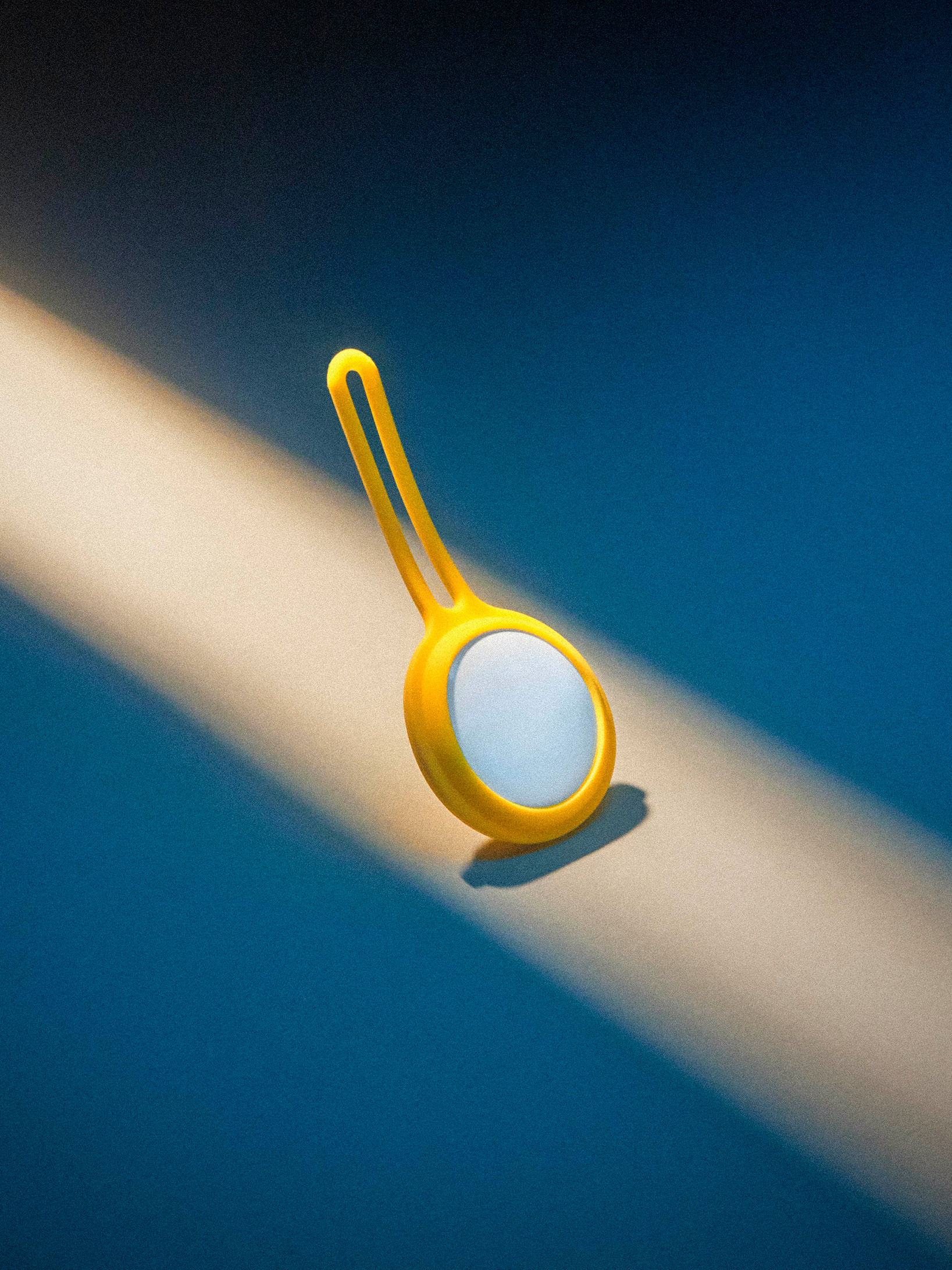 Apple air tag in a yellow rubber holder in a beam of light on a blue background