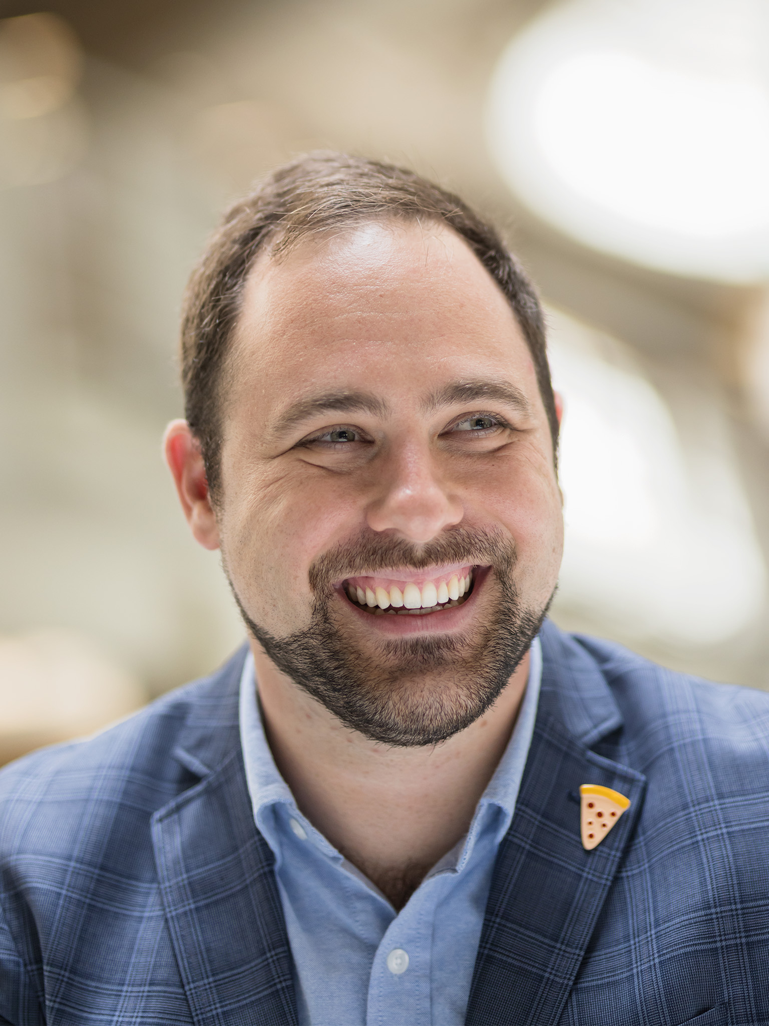 Alexander Hughes, smiling, wearing a pizza pin on his jacket lapel