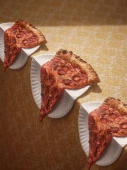 photograph of 3 pizza slices on paper plates drooping off of the edge of a table