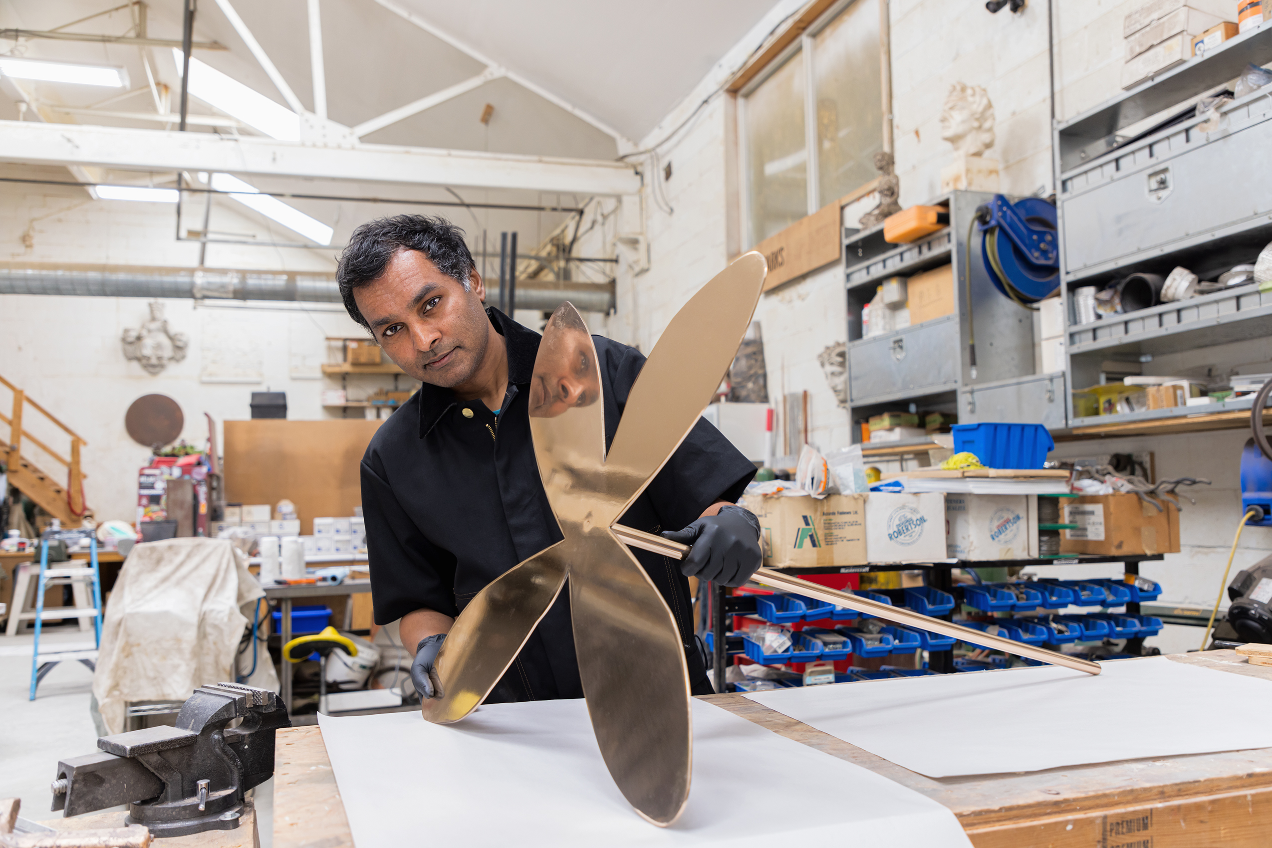 Andil Gosine behind a work table holding a bronze sculpture